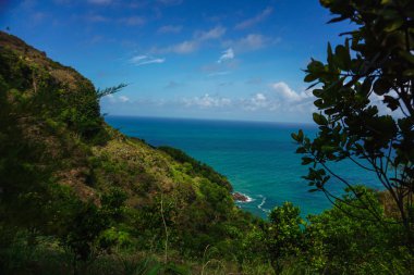 Arka planda dik tepe ve okyanus olan tropik bir manzara. Kebumen, Merkez Java, Endonezya