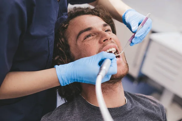 Bir ağızlık ve mükemmel beyaz dişler dentis sandalyeyle genç bir adam portresi var bir yordam oral hijyen çok dikkatli bir şekilde çalışan diş hekimi ar — Stok fotoğraf