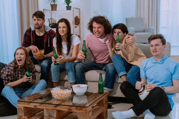 Крупним планом велика група друзів у вітальні дивиться футбольний матч перед телевізором дуже зосереджений харизматичними обличчями, що їдять попкорн і п'ють пиво — стокове фото