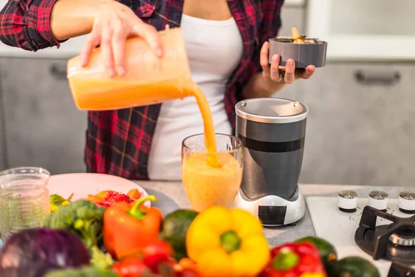 Detalhes de close-up no casal da cozinha pela manhã derramando um smoothie laranja saudável em um copo grande — Fotografia de Stock