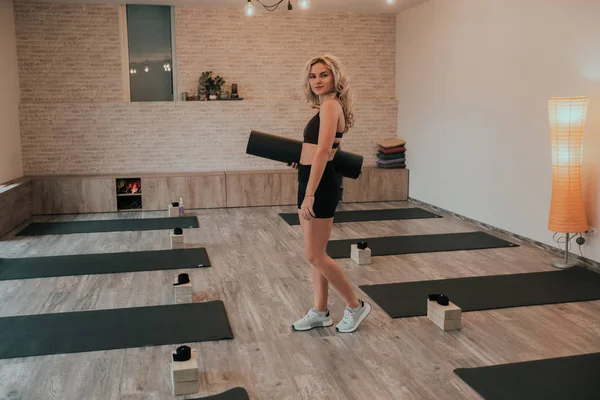 Kıvırcık saçlı pretty sarışın bayan o parlak bir stüdyoda yoga meditasyon başlatmak için hazırlamak kameraya düz bakıyor