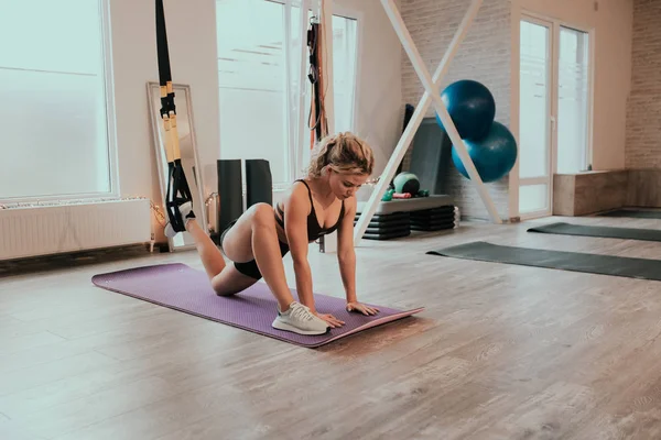 En un luminoso estudio de yoga señora concentrada practicando el estiramiento del cuerpo y las piernas utilizando un soporte especial elástico, lleva puesta una ropa deportiva — Foto de Stock