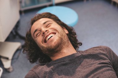 Dudaklarında gülümseme olan hasta doktorun gelip dişlerinin prosedürüne başlamasını bekliyor.