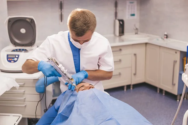 Doktor bir modern kliniğinde sandalyede döşeme ve başlamak için bekleyen bir mikro ihtiyaç duyan, genç hasta bir vampir facelift yordam için hazırlanıyor