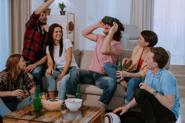 Велика компанія з багатьох етнічних друзів у вітальні вони мають кумедний час разом, пані, використовуючи окуляри віртуальної реальності, щоб досліджувати світ, який вона дуже вражена — стокове фото