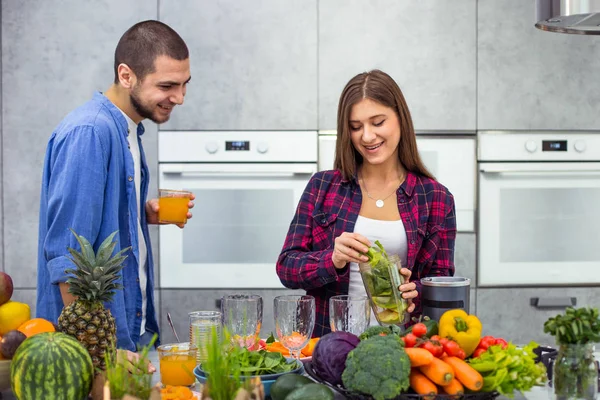Café da manhã saudável para um jovem casal de manhã, homem bebendo suco de laranja e senhora preparando o smoothie em uma cozinha moderna — Fotografia de Stock