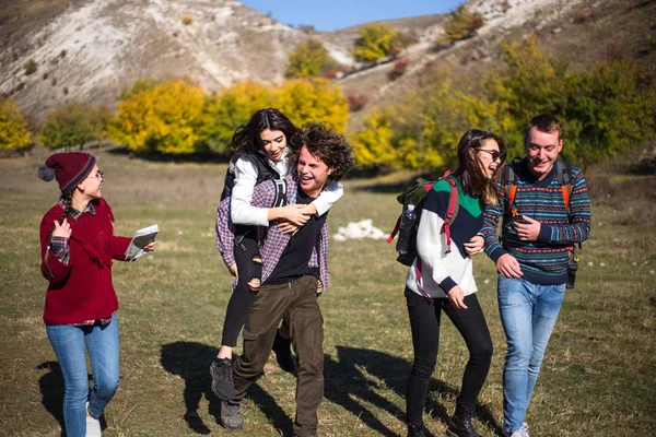 Щаслива група друзів мультикультурна гарно подорожуйте разом у горах, посміхаючись, ходячи і беручи один з одним — стокове фото