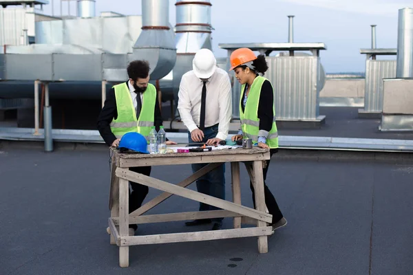 Grupo multiétnico de engenheiros de trabalhadores arquitetos capataz analisando o plano de canteiro de obras no telhado do edifício moderno — Fotografia de Stock