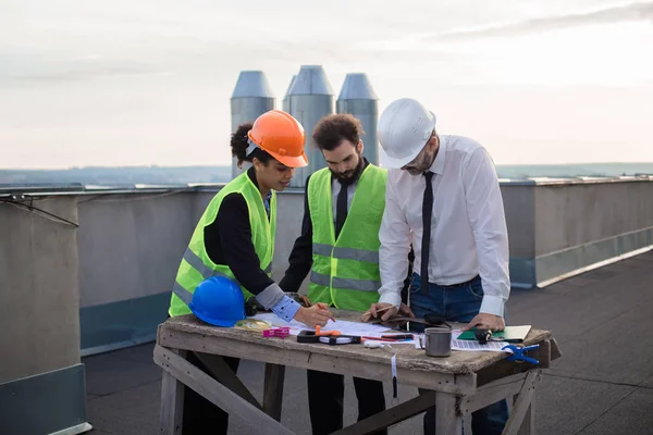 Bel gruppo multietnico di lavoratori in un cantiere moderno analizzando il piano di costruzione indossano i caschi di sicurezza — Foto Stock