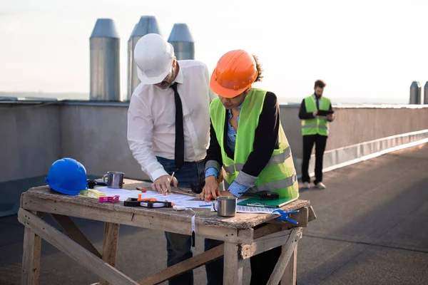 In un moderno cantiere sul tetto bella ingegnere donna africana con l'architetto analizzando il piano di cantiere altro un altro ingegnere guardando in tablet — Foto Stock