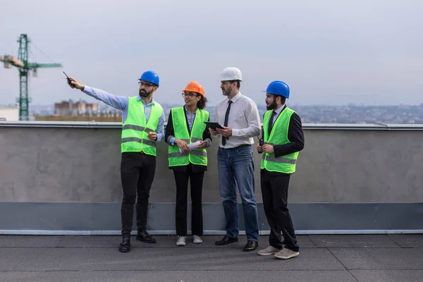 Şantiye mühendisi mimarlar ve foreman bir tablet kullanarak şantiye planı analiz ve güvenlik kask giyen çok ırklı işçilerin bir grup