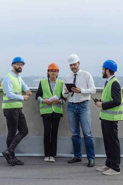 Grupo multiétnico de engenheiros de trabalhadores arquitetos capataz analisando o plano de canteiro de obras no telhado do edifício moderno . — Fotografia de Stock