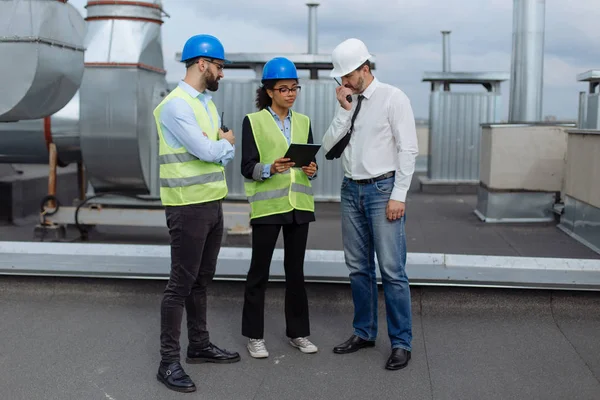 Bel gruppo multietnico di lavoratori in un cantiere moderno analizzando il piano di costruzione indossano i caschi di sicurezza — Foto Stock