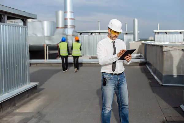 No telhado do engenheiro do canteiro de obras faça uma conversa com algum trabalhador usando o tablet — Fotografia de Stock