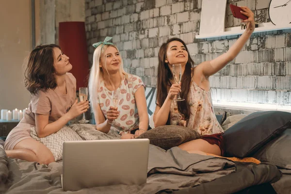 Damas jóvenes multiétnicas tomando selfies en un dormitorio moderno, tienen una fiesta de pijamas celebrando las copas de champán y disfrutan del tiempo con sus amigos —  Fotos de Stock