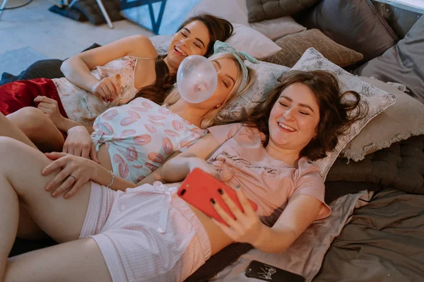 Muy carismáticos tres señoras tomando divertidos selfies mientras utilizan el teléfono inteligente delante de la cámara que sonríe a lo grande y disfrutar del tiempo juntos —  Fotos de Stock