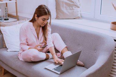 Hoş bir oturma odası kanepe oturma ve bir pijama giymiş bir dizüstü bilgisayar üzerinde çalışan güzel bir genç bayan