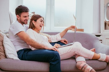 Güzel genç çift kanepede oturan ve notebook üzerinde bir şey sabah gülümseyerek, onlar are her ikisi pijama