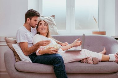 Mutlu zaman birlikte kendi oturma odasında pijama genç bir çift harcama, kanepede oturan ve dizüstü bilgisayarda bir şey izlerken