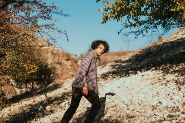 Genç bir adam kameraya bakar, bir tepeye çıkar.