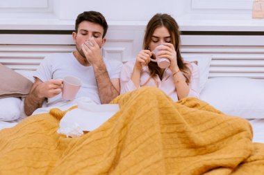 Sabah öksürük çift bir grip ve burun akıntısı adam bir fincan sıcak bir şey içme ve burun için doku kullanarak burun akıntısı var