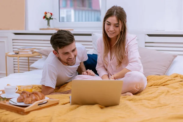 Una pareja joven ve videos divertidos en el portátil, sonríen y se divierten —  Fotos de Stock