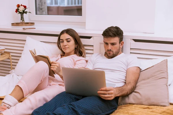 Primer plano de una joven pareja pasando un buen rato juntos en una cama acogedora, mujer y hombre leyendo —  Fotos de Stock