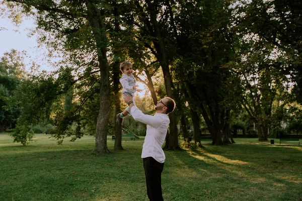 En medio de un parque verde papá tomando a su hijo en sus brazos y se dio la vuelta juntos disfrutando del tiempo que pasamos juntos —  Fotos de Stock