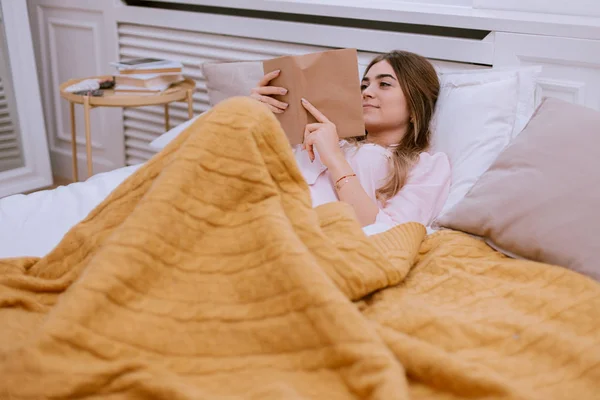 Mujer leyendo un libro mientras está acostada en la cama, diseño moderno alrededor —  Fotos de Stock