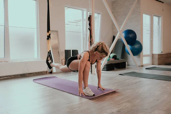 En un luminoso estudio de yoga señora concentrada practicando el estiramiento del cuerpo y las piernas utilizando un soporte especial elástico, lleva puesta una ropa deportiva — Foto de Stock