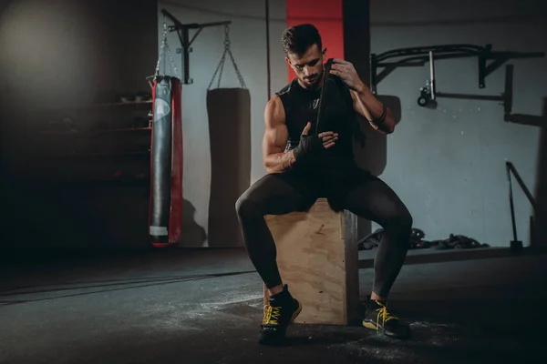 Attractive guy concentrated using a professional bandages wraps his hands preparing to start his training on the gym class — Stock Photo, Image