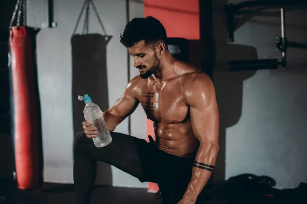 Detalles abs cuerpo atlético chico sosteniendo una botella de agua en una clase de fitness cruz que quiere beber un poco de agua después de su intenso entrenamiento — Foto de Stock