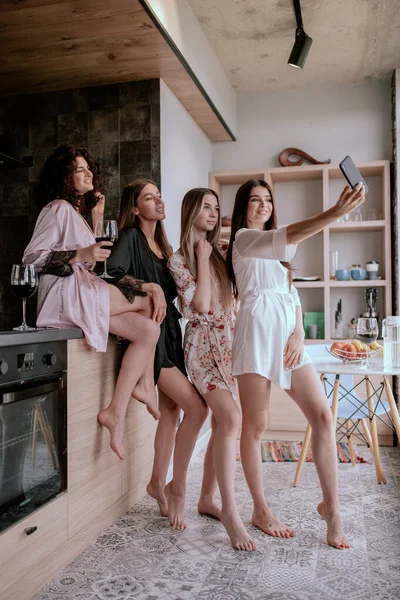 Pleased girls in pajamas having fun in kitchen, Cheerful young lady making selfie in morning with friends — ストック写真