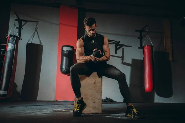 Attractive guy concentrated using a professional bandages wraps his hands preparing to start his training on the gym class — Stock Photo, Image