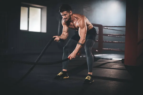 Ejercicios duros con cuerdas hombre atlético practicando entrenamiento de cross fit hace cara concentrada mientras hace su entrenamiento — Foto de Stock