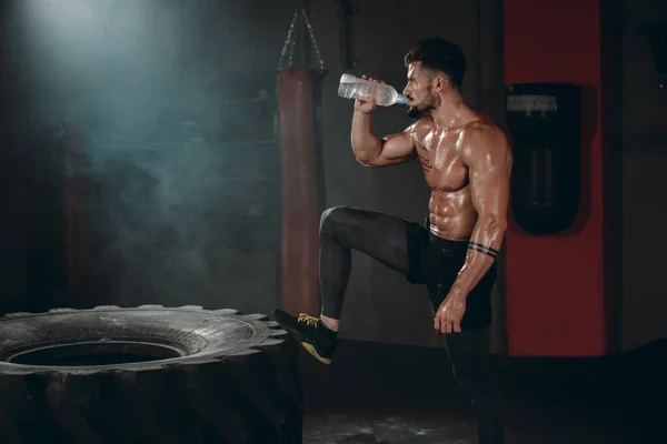 Dorstig fit lichaam man na een cross fit workout drinken van wat water uit een plastic fles — Stockfoto