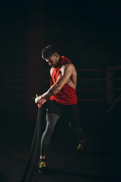 Atractivo chico musculatura entrenamiento en una clase de fitness cruz utilizando cuerdas concentradas haciendo su entrenamiento — Foto de Stock