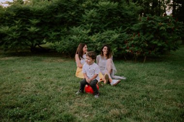 Çok sevimli iki yıl çocuk arka planda iki bayan büyük gülümseyen ve parkta harcama zaman zevk ise kamera önünde komik yüzler yapmak