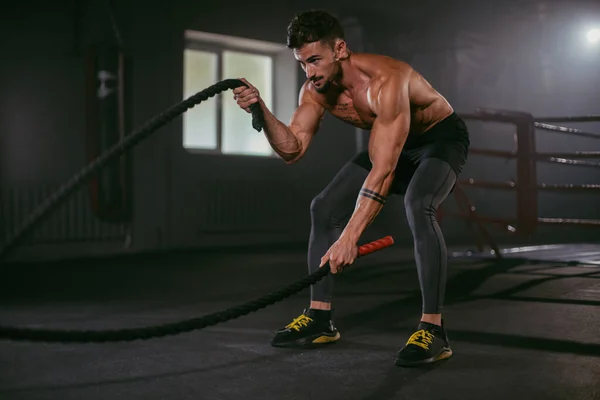 Ejercicios duros con cuerdas hombre atlético practicando entrenamiento de cross fit hace cara concentrada mientras hace su entrenamiento — Foto de Stock