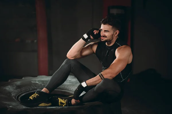 En la clase de gimnasia chico atlético bien parecido hablando en su teléfono después de un duro entrenamiento ejercicios que tienen una cara feliz y sonriente — Foto de Stock