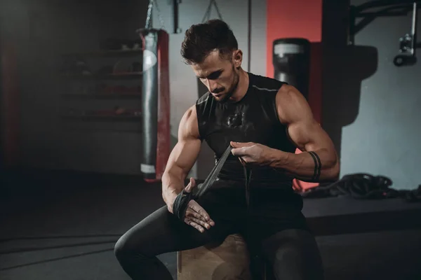 Portret geconcentreerde brutale atletische kerel wraps handen met behulp van de professionele bandages zittend op de stoel in de sportschool klasse — Stockfoto