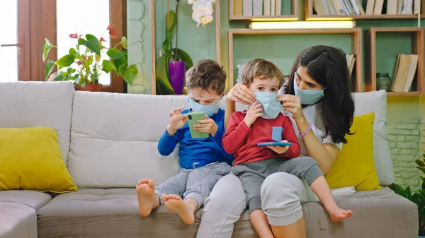 W kwarantannie matka z dziećmi dbaj o mamę w masce ochronnej do jej małego syna podczas siedzenia na kanapie przed kamerą, podczas gdy jest koronawirus 2019 — Zdjęcie stockowe