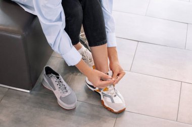 Kanepedeki ayakkabı dükkanındaki bayan. Renkli spor ayakkabıları giyen yeni bir çift deneyin.