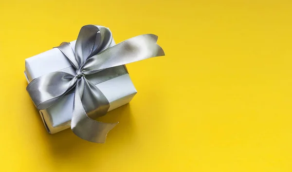 White box with a gift and silver flying on a yellow background. Festive background