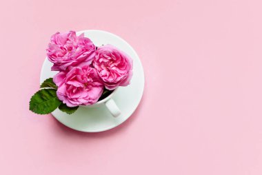 Pembe arka planda bir kasede üç pembe gül. Kartpostal şablonu. Şenlik arka planı. Düz yatıyordu