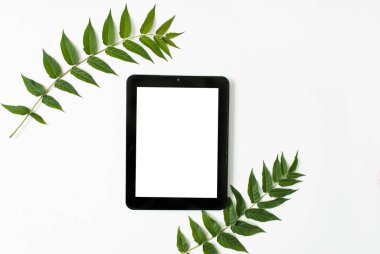 Beyaz arkaplanda yeşil yapraklar ve tablet var. İş yeri konsepti. Mesaj için yer. Düz yatıyordu. Üst Manzara. maket yap
