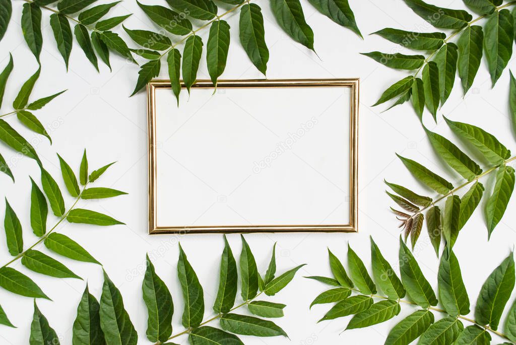 Stylish modern composition. Golden empty frame and green tropical leaves on a white background. Flat lay. Mock up