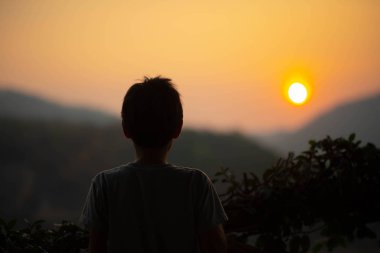 Tepenin arkasında gündoğumu sabah isteyen küçük çocuk