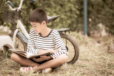 Parkta bisikletle oturan küçük çocuk kitap okuyor