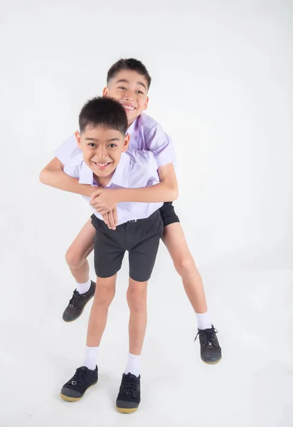 小亚洲兄弟姐妹男孩在学生制服一起摆姿势在白色背景 免版税图库照片